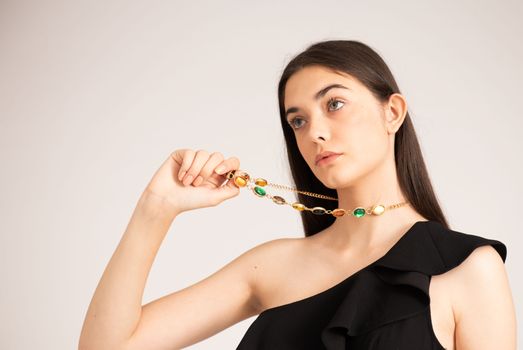 Portrait of a stylish woman in a black dress holding colorful jewelry.
