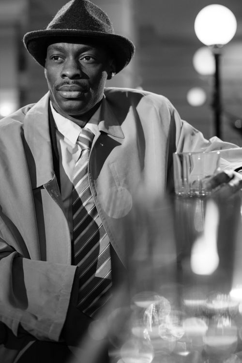 Free Black and white photo capturing a classic noir detective scene with a man in a trench coat and fedora. Stock Photo