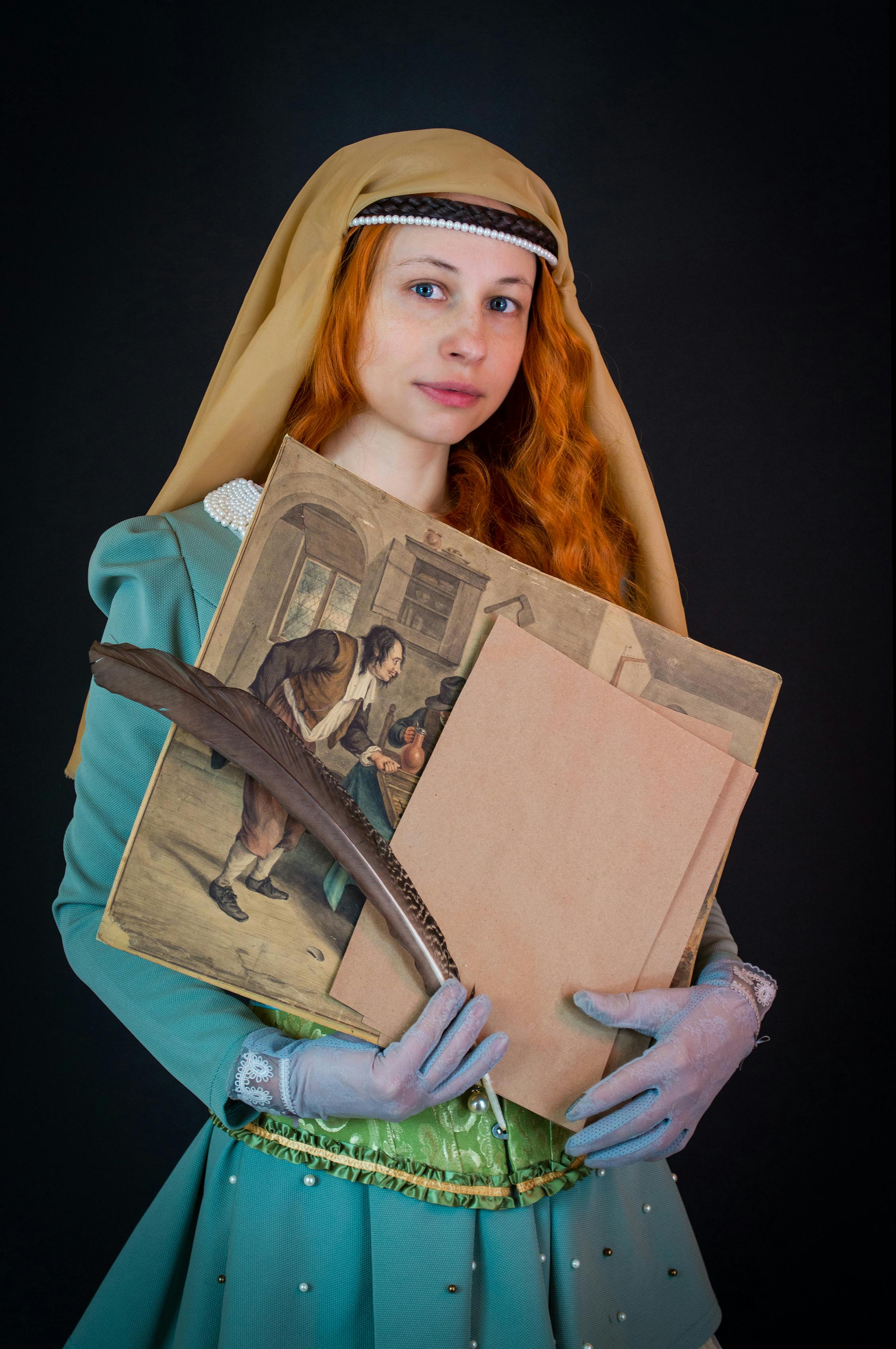 Charming ginger female in colorful vintage clothes and gloves with picture and feather standing against black wall in studio