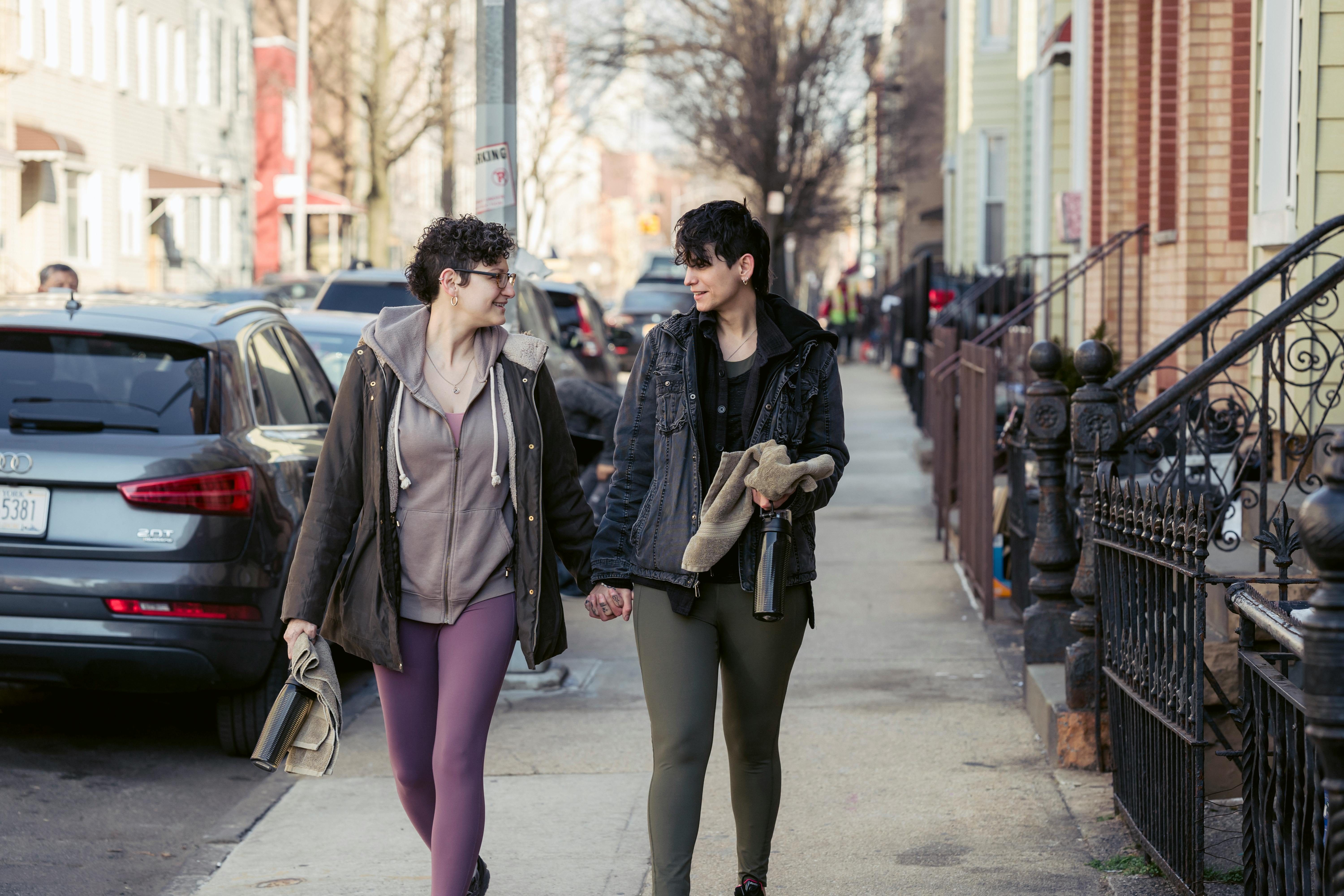 lesbian couple holding hands while walking in street near buildings