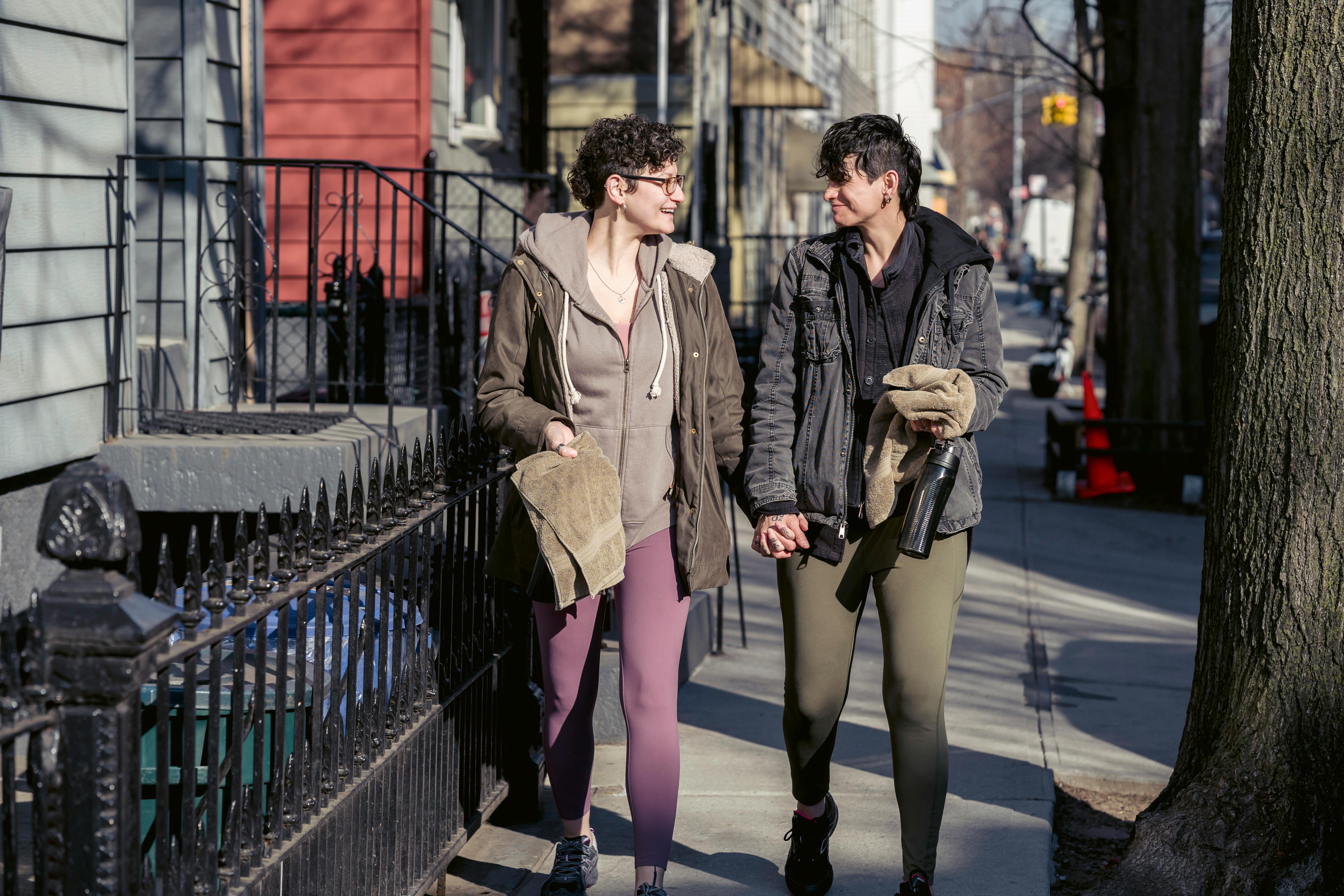 cheerful lesbian couple holding hands and strolling on city street