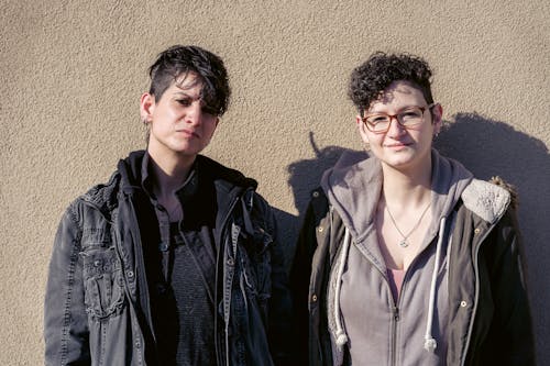 Adult lesbian couple in outerwear standing on sunny street