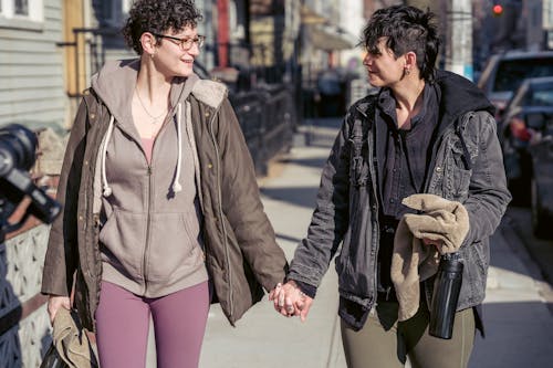 Cheerful lesbian sportswomen holding hands and strolling on street