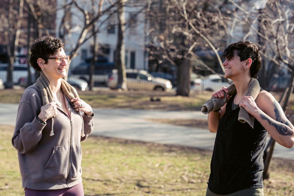 Cheerful friends with short dark hair looking at each other and smiling on blurred background of alley in park
