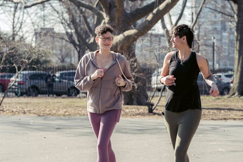 Free Positive sporty friends in activewear running on asphalt pavement on blurred background of park Stock Photo