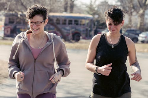 Glad women in sportswear jogging on sunny street