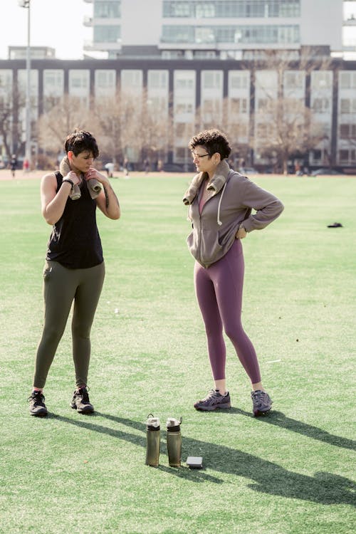 Full body of sportswomen doing warm up on grass of lawn on blurred background of house in town