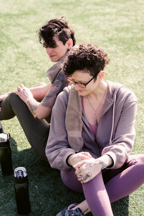 Free From above of couple of athletic girlfriend bending knee while stretching and relaxing on grass in daytime Stock Photo