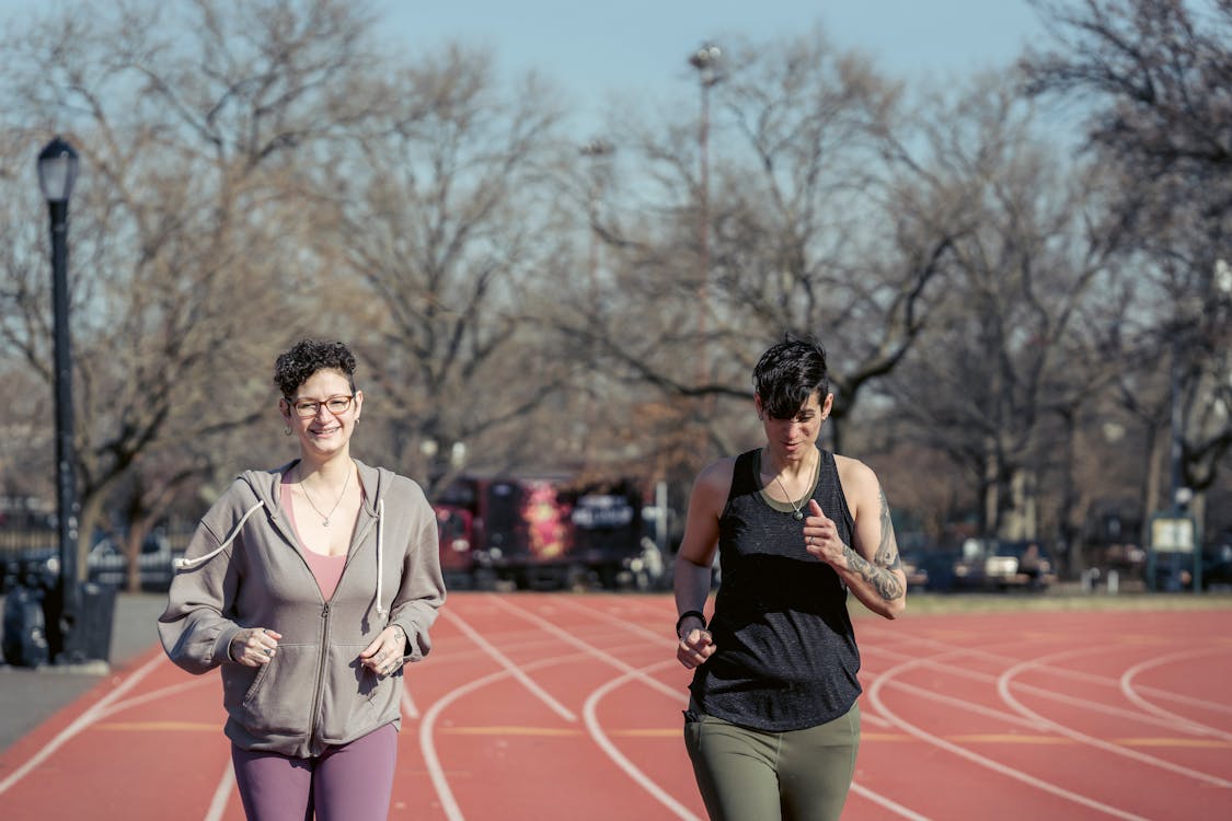 Free Smiling sportswomen running on track in sunlight Stock Photo