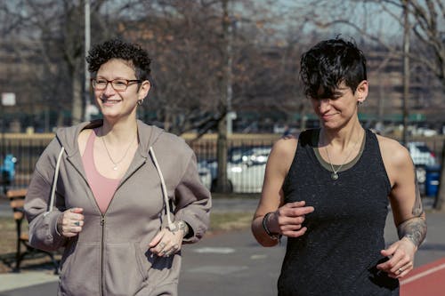 Free Modern females in sportswear running on stadium track and smiling while training on street together in autumn in daylight Stock Photo