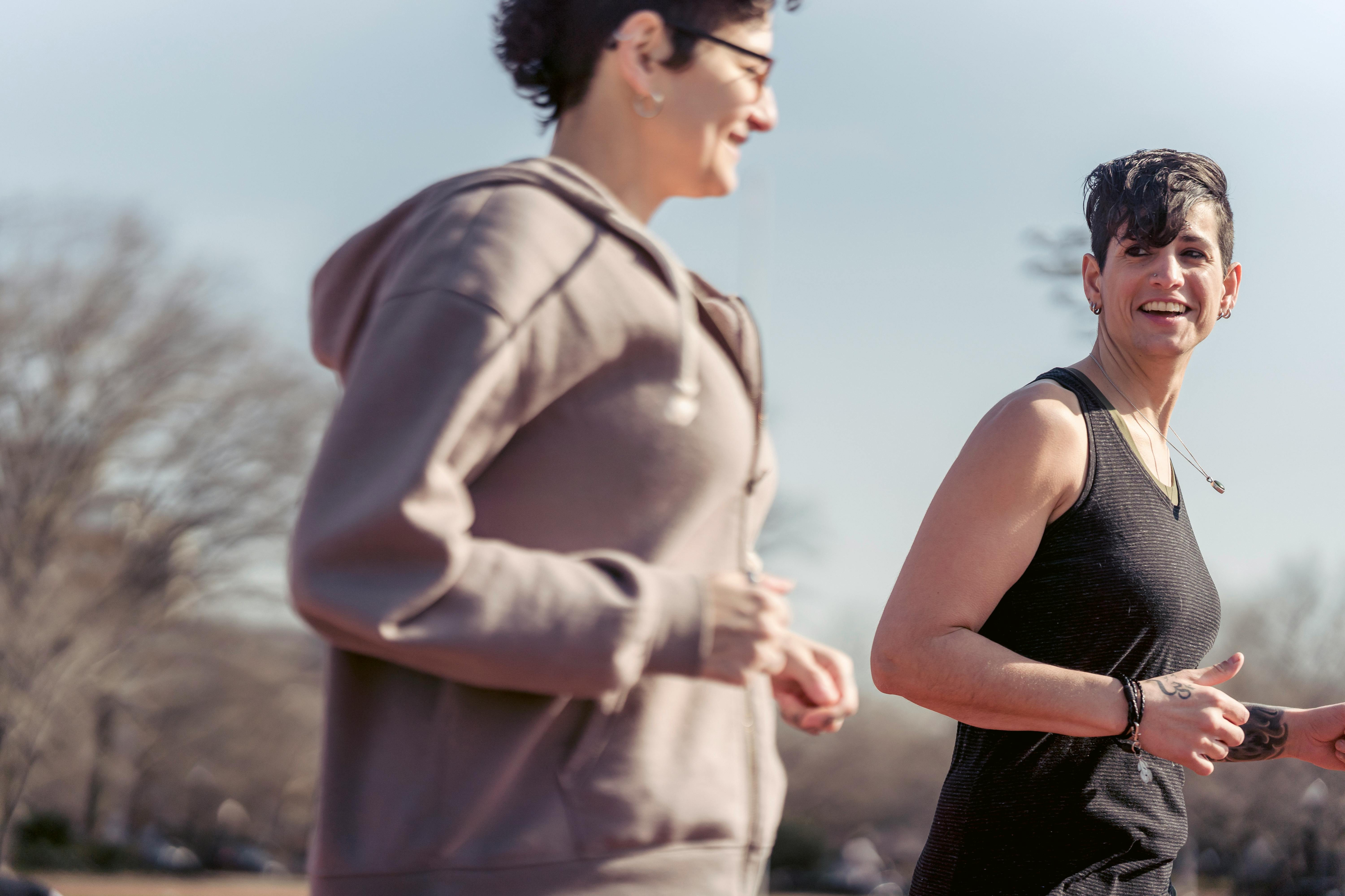 Side view of crop female athlete talking with smiling androgynous female while jogging to be in good shape and to keep healthy lifestyle