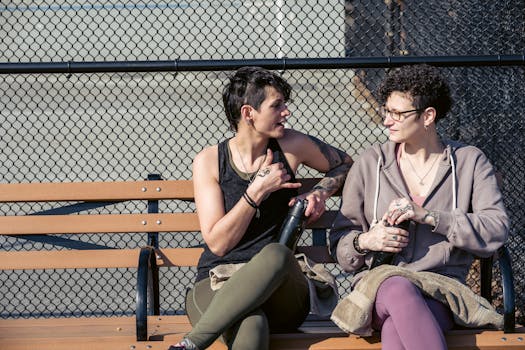 Two women sitting on a bench having a casual conversation outdoors.