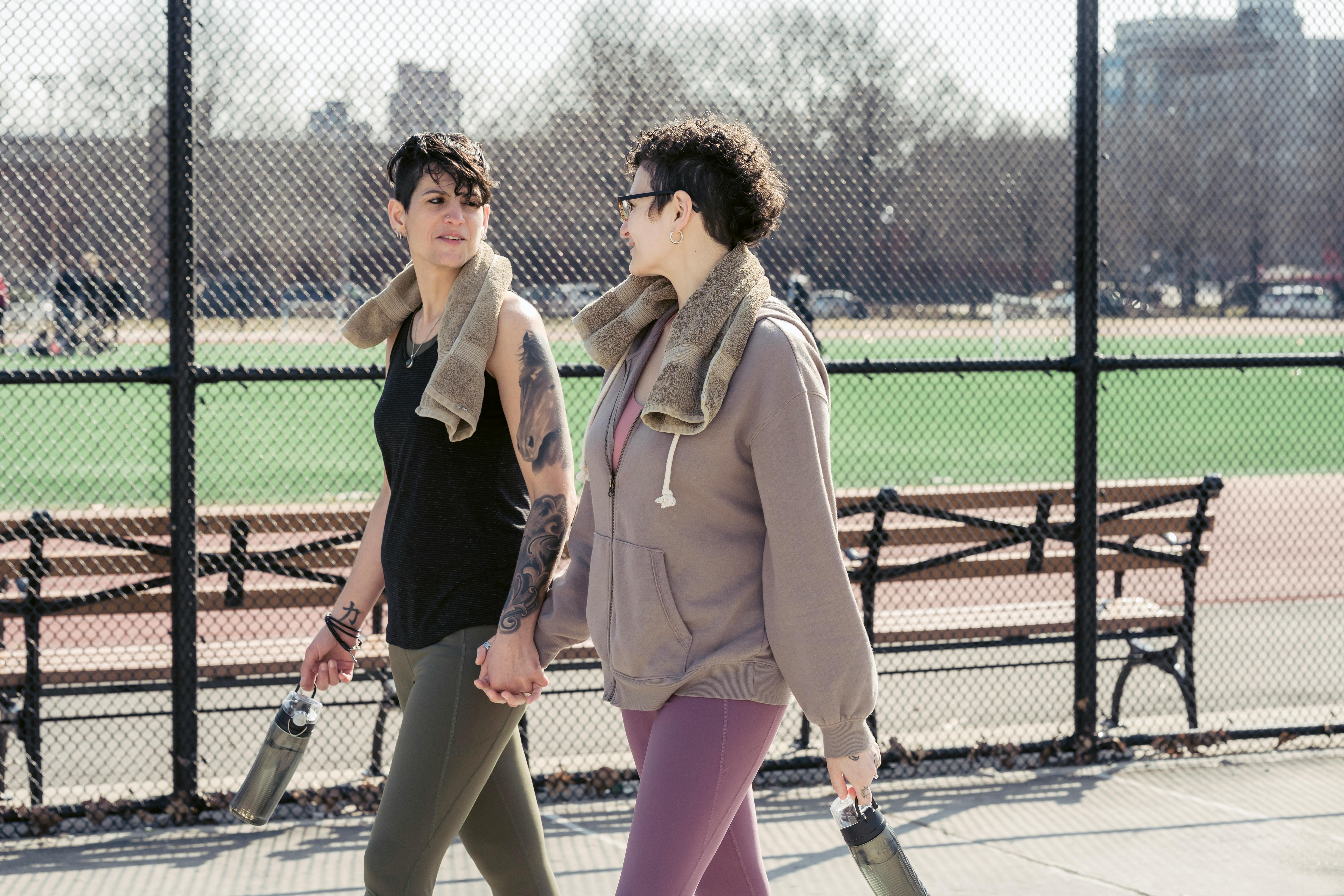 delighted girlfriends passing by sports ground while chatting