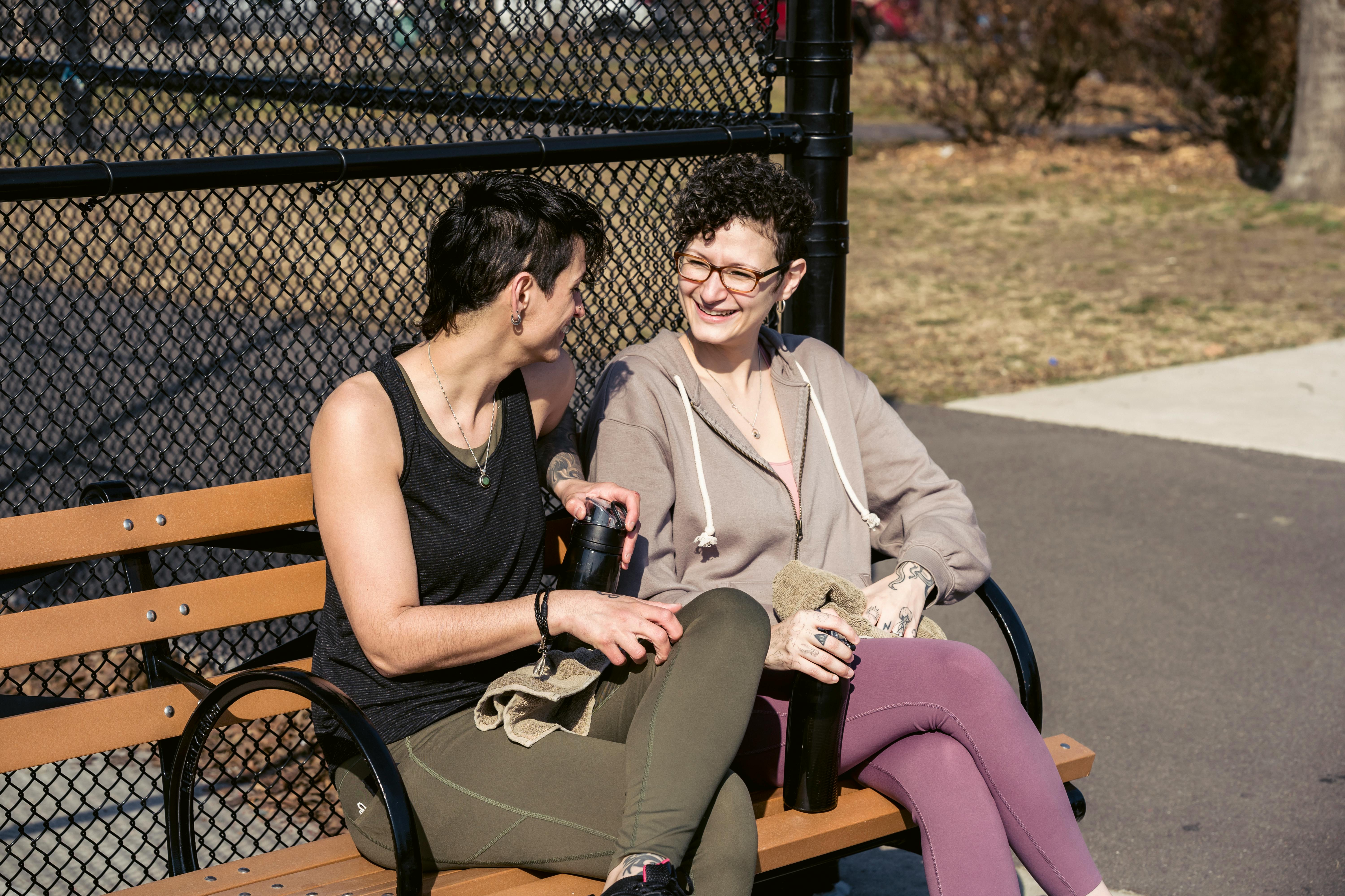 happy sportswomen speaking on bench after training in park