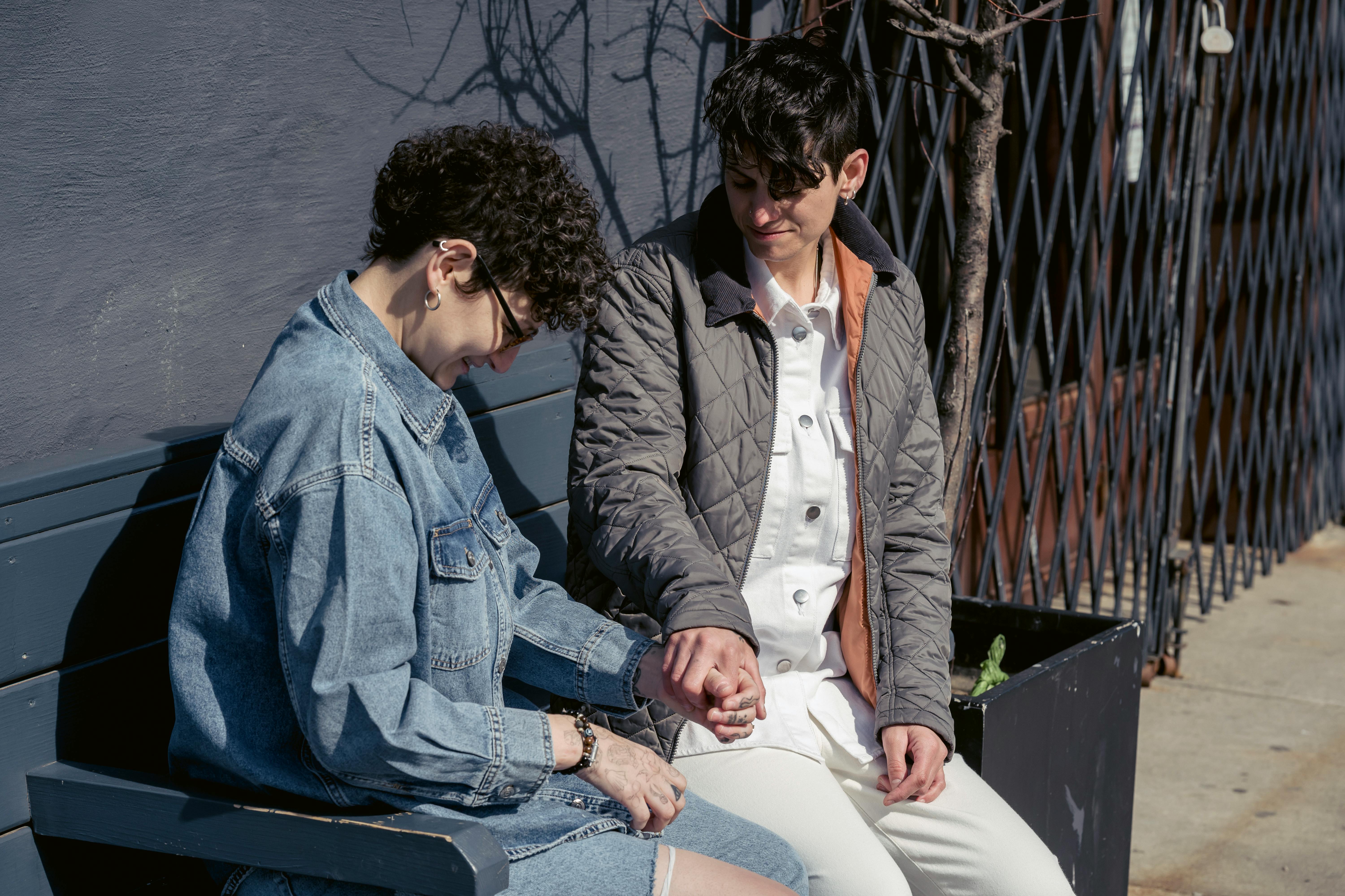 happy young homosexual women holding hands and smiling on street bench