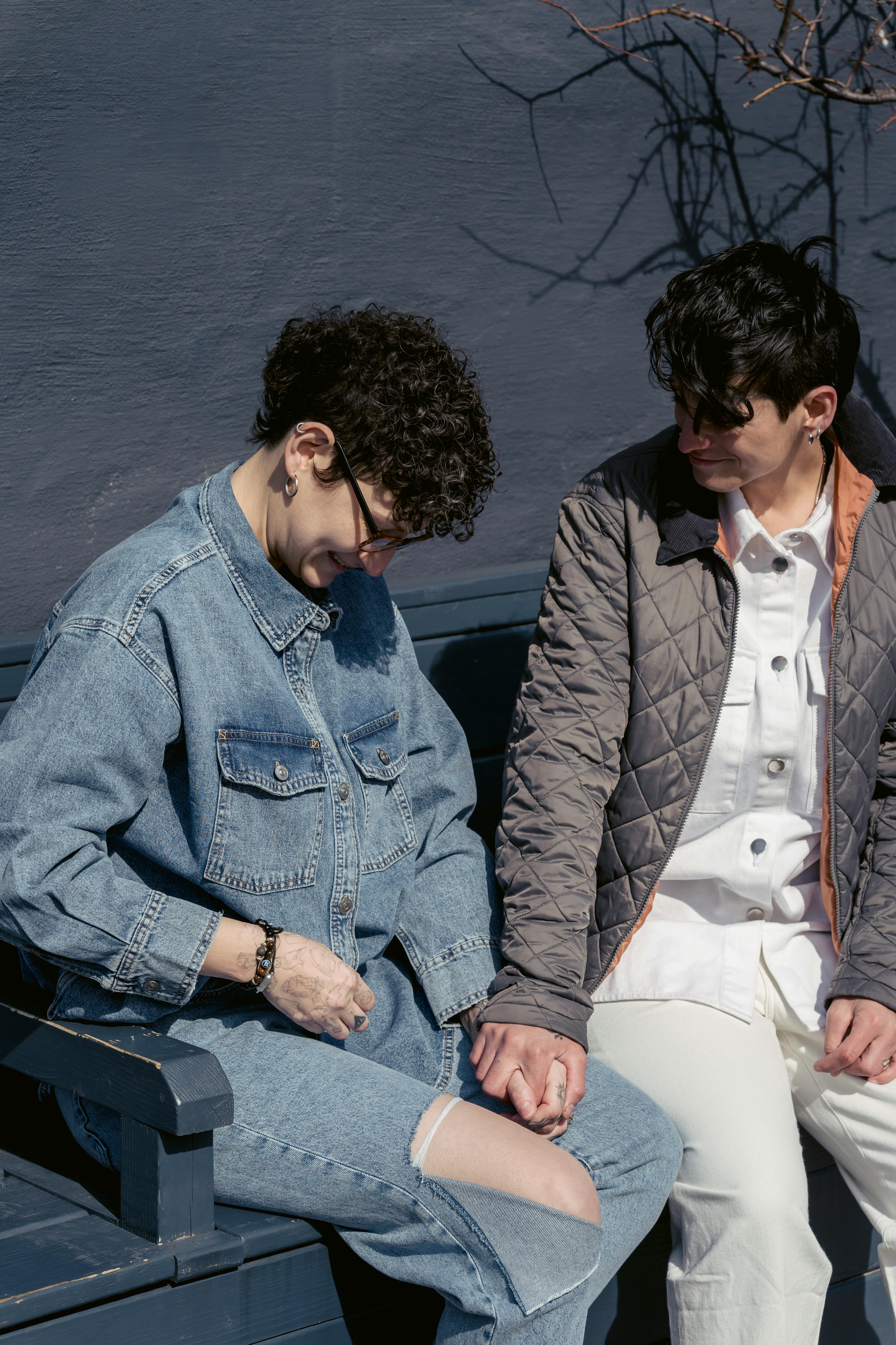 happy young lesbian couple holding hands while sitting together on bench in city