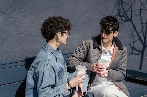 Free Delighted young women chatting and drinking coffee on bench Stock Photo