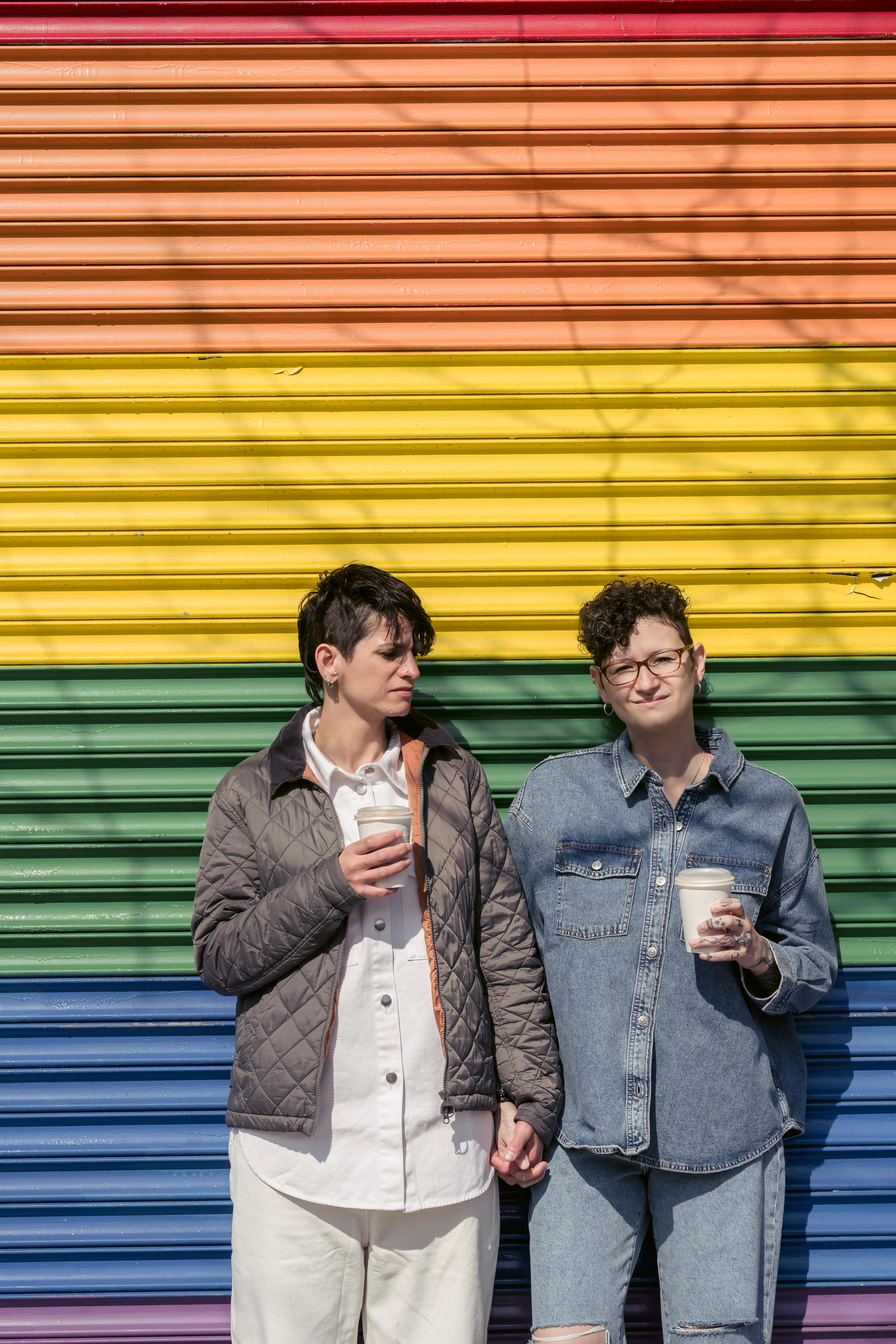 cool lesbian couple drinking coffee on street near colorful wall