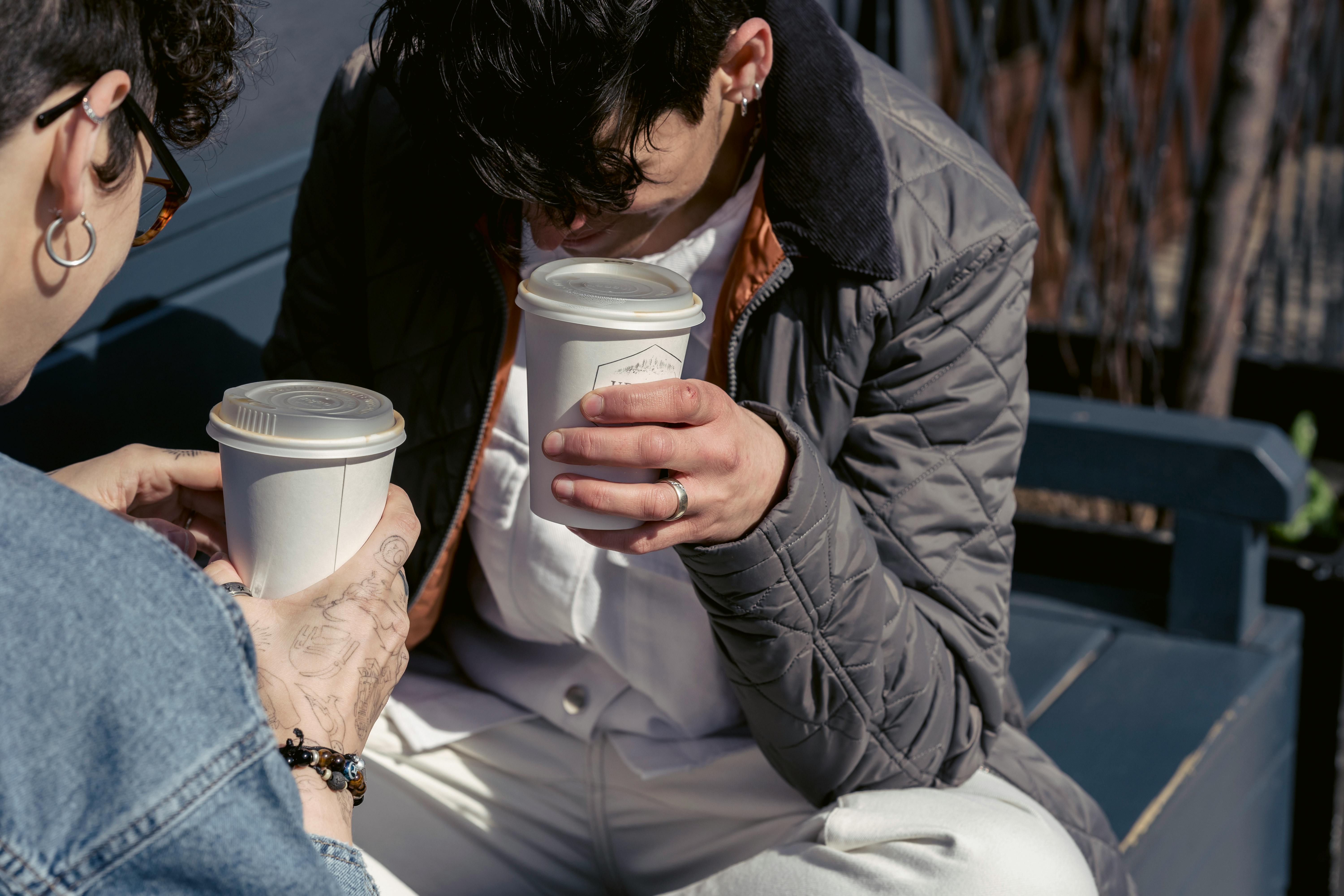 cheerful young women drinking coffee to go and laughing on bench