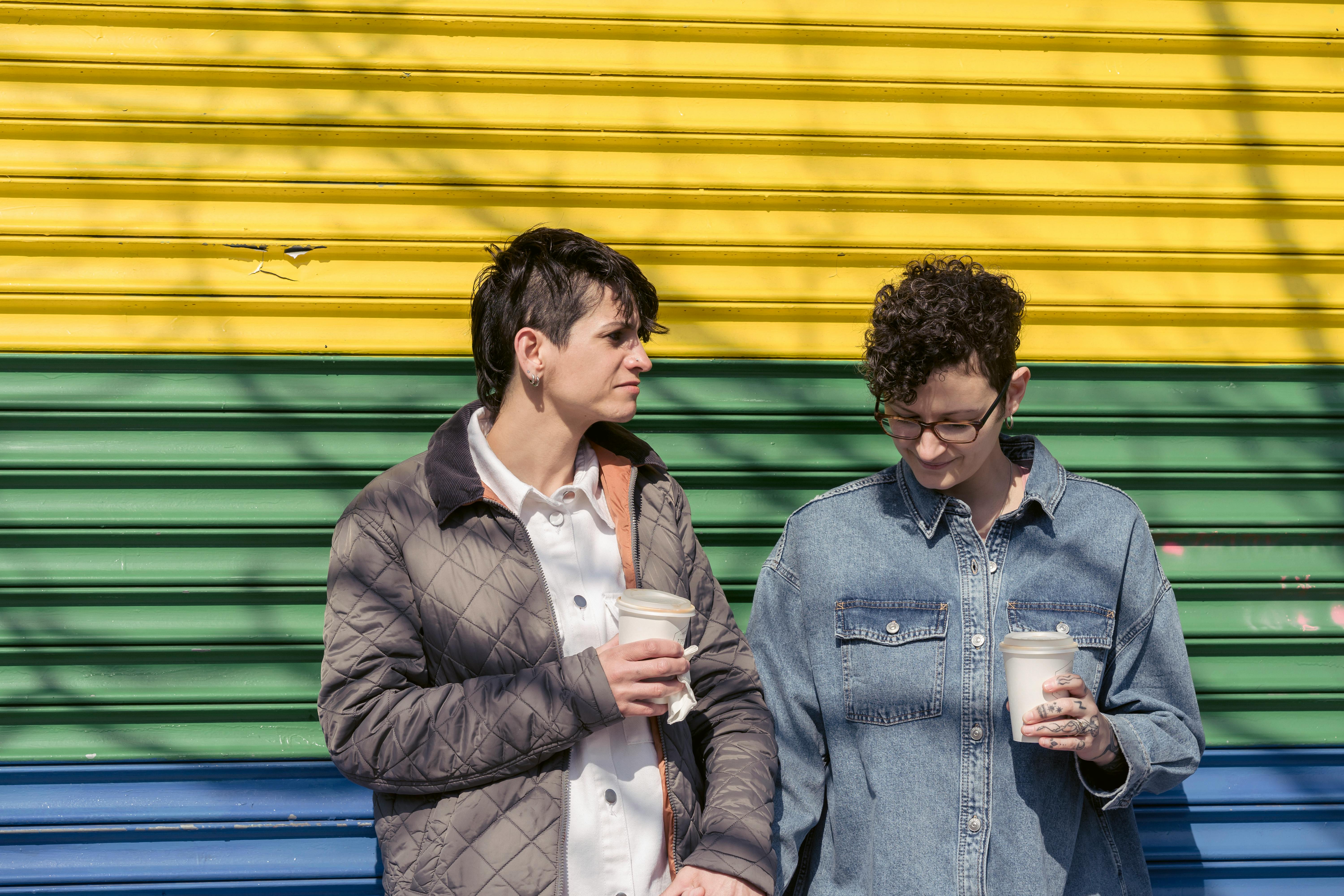 content young lesbians holding hands and drinking takeaway beverages on street