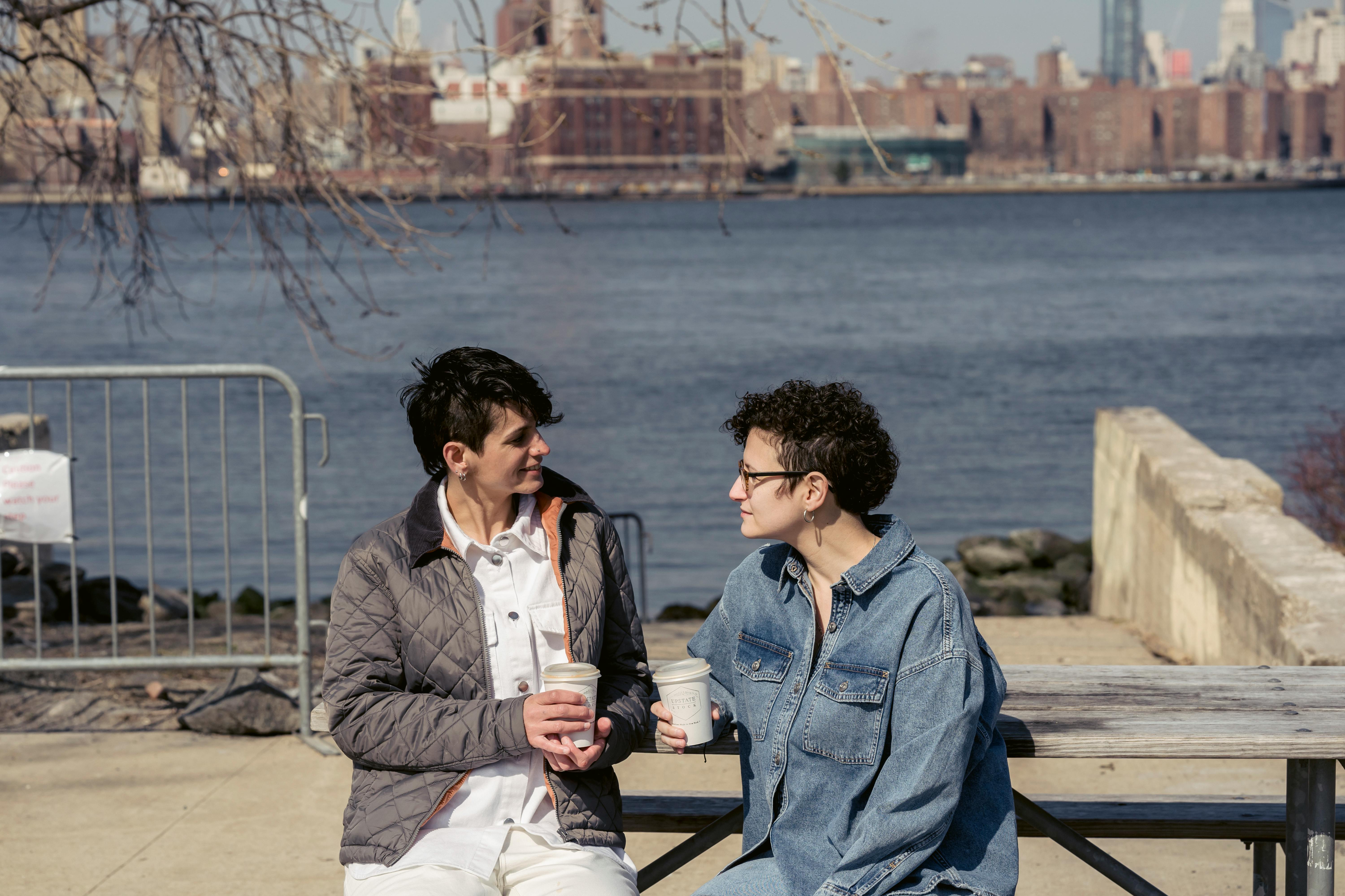 young female friends chatting on waterfront during coffee break