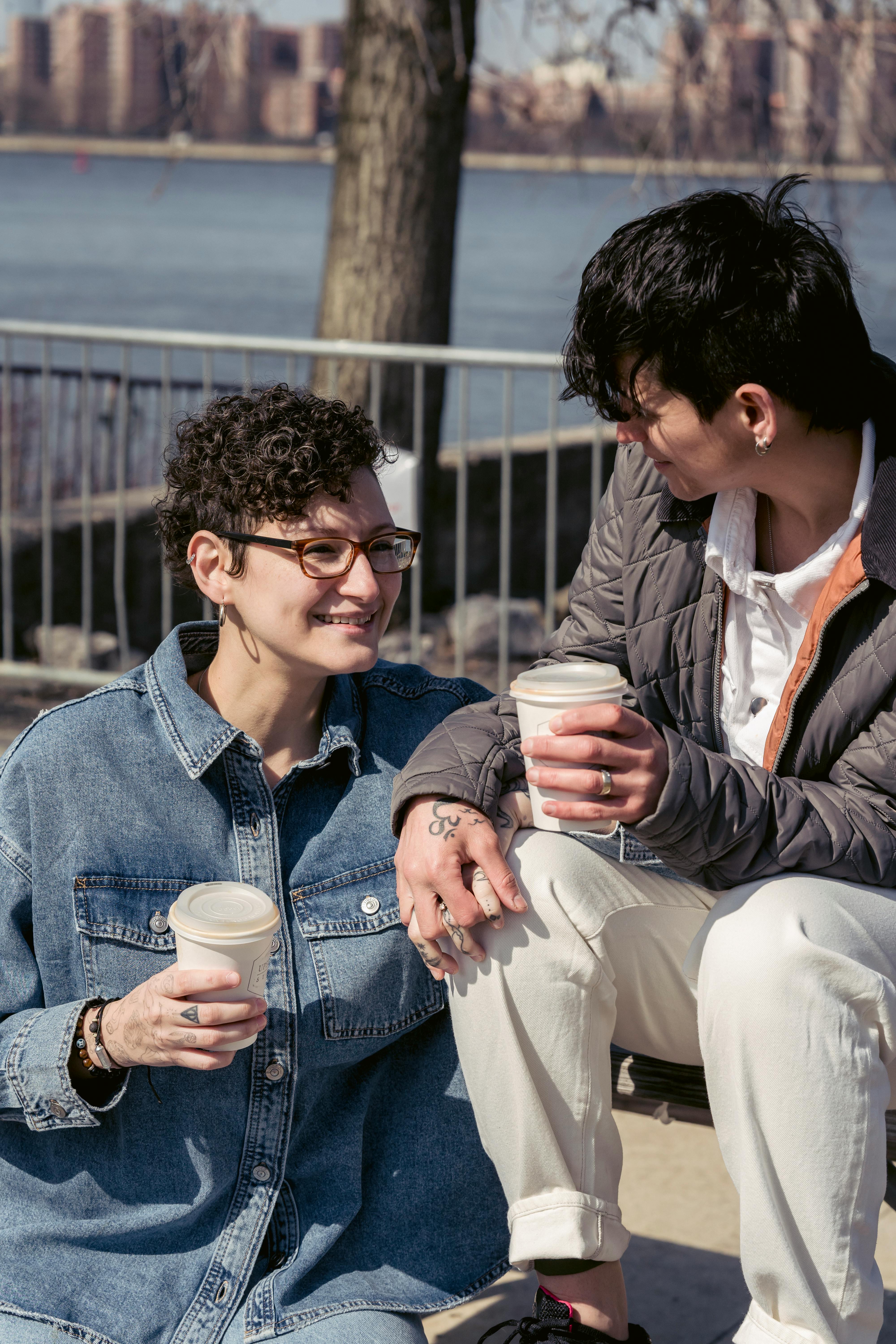 beloved lesbians holding hands and drinking coffee near river in city