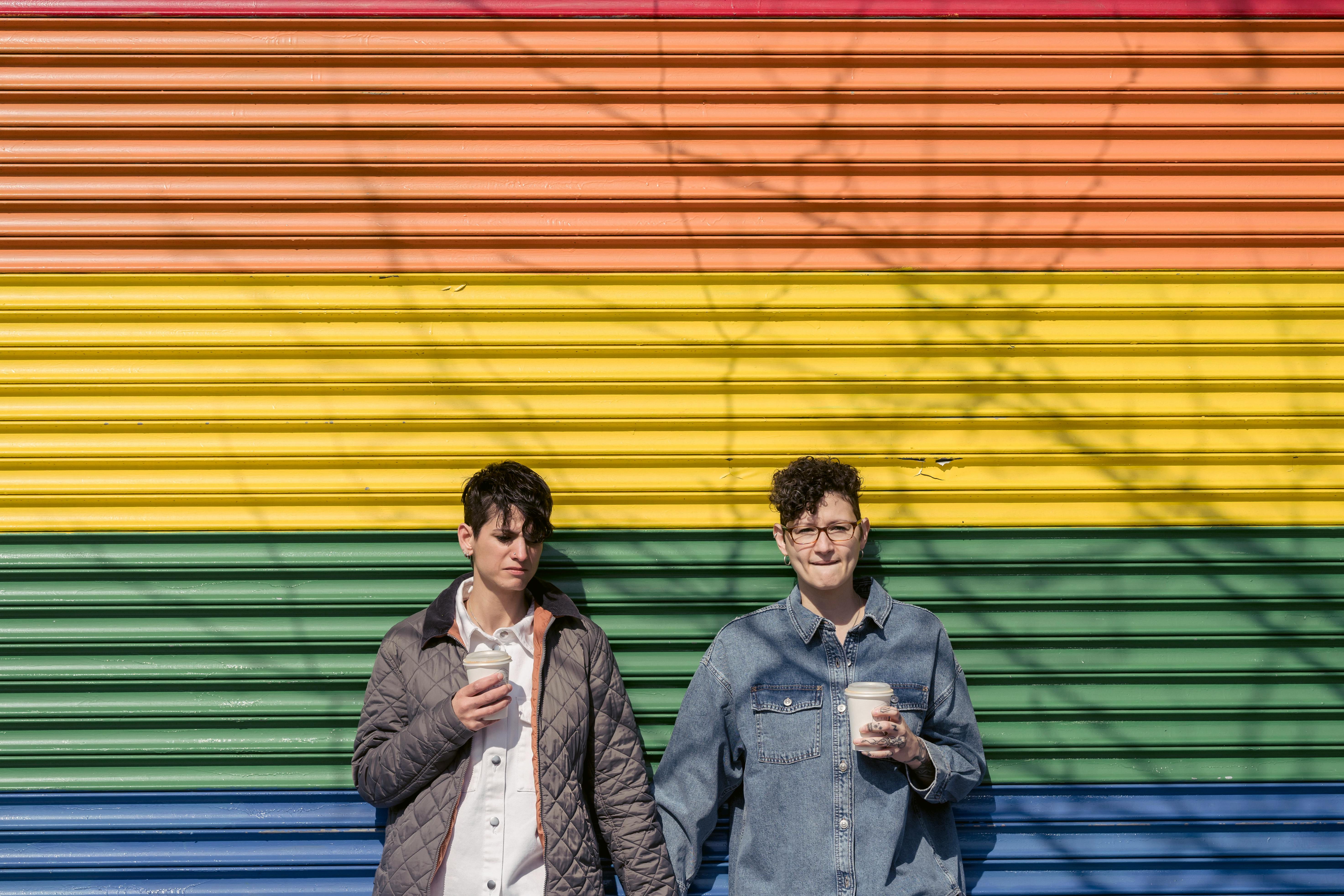 young girlfriends drinking takeaway beverages near multicolored wall