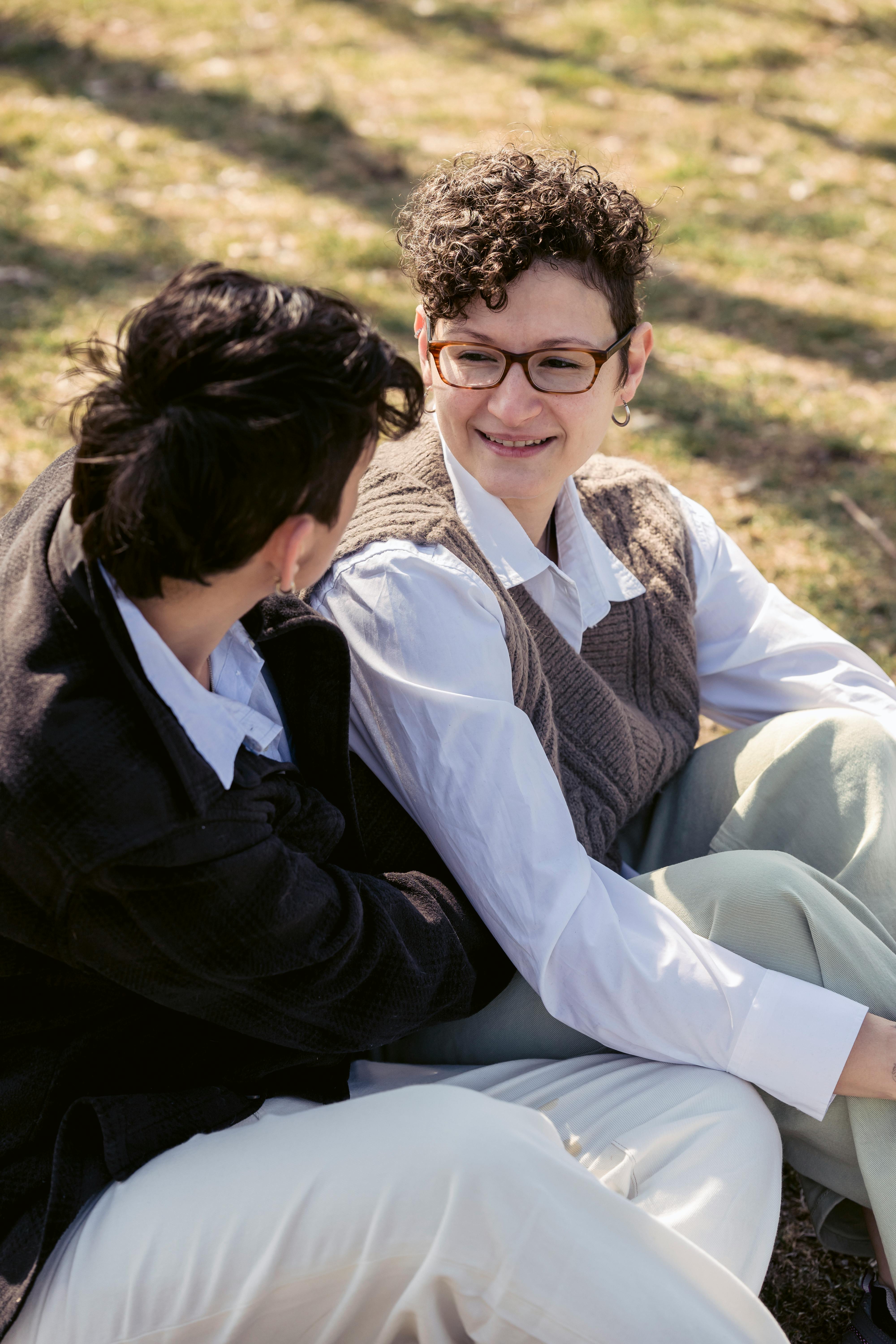 positive ladies relaxing on lawn in park and chatting