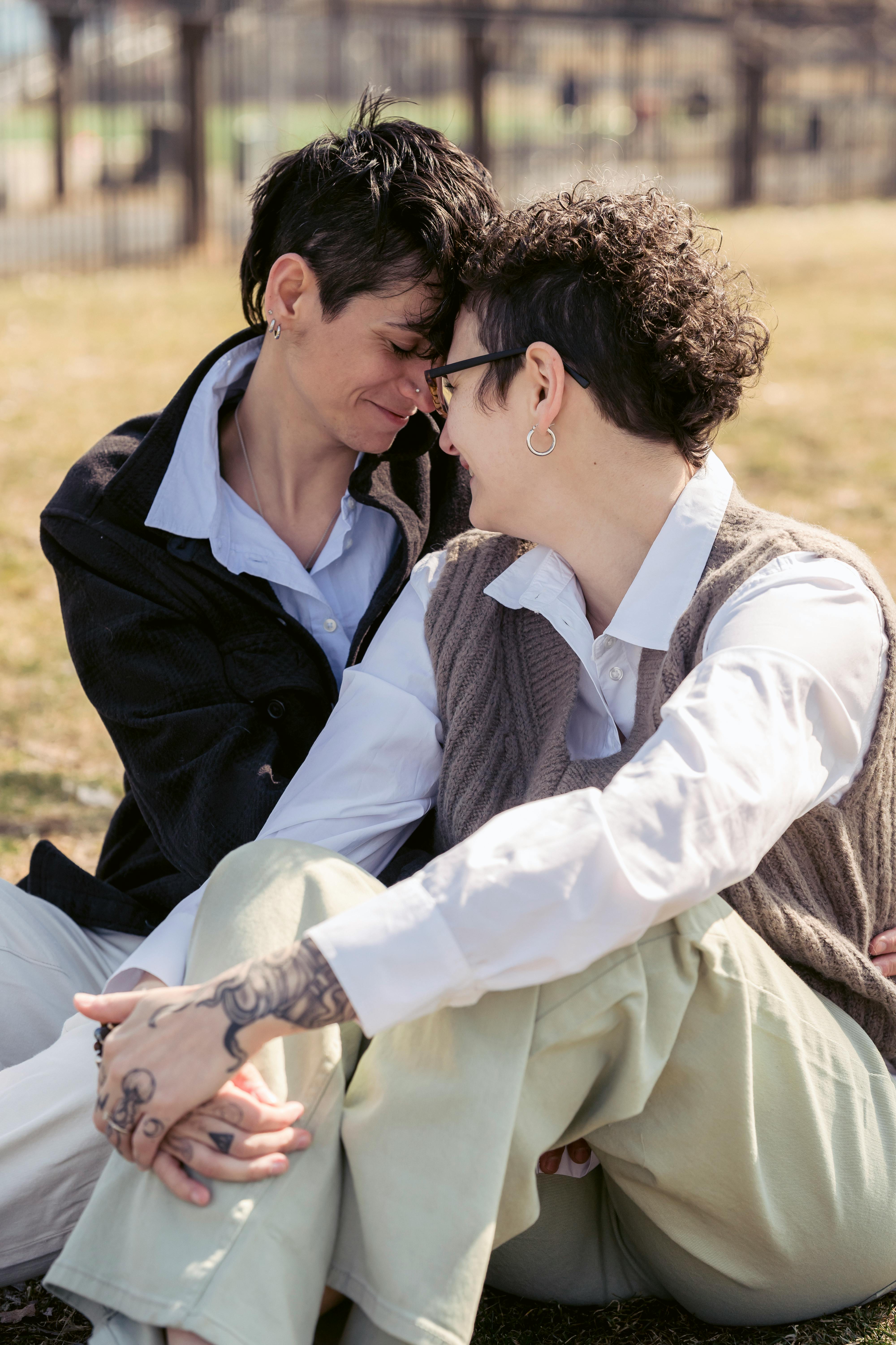 happy lesbian couple touching foreheads sitting on lawn in sunlight