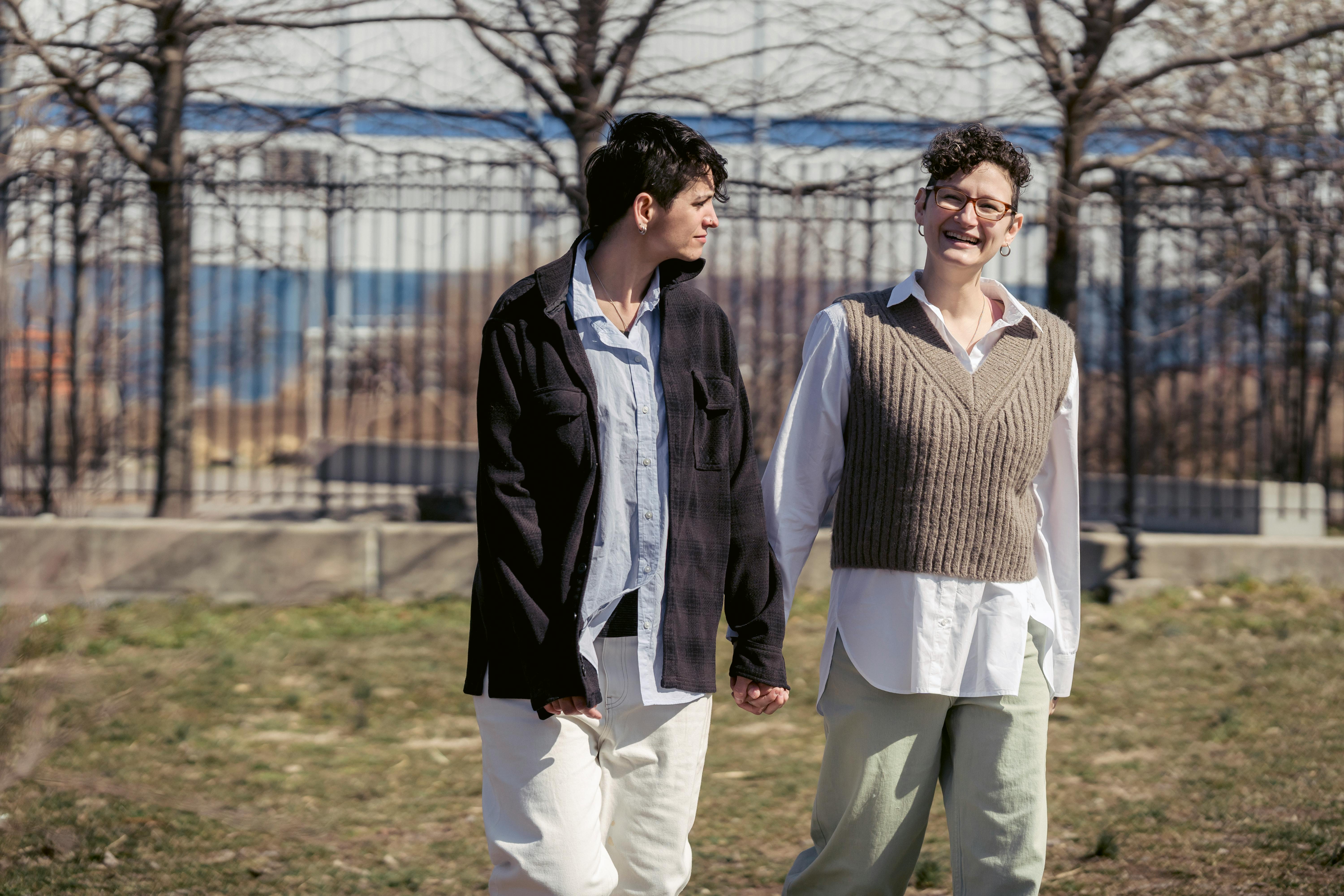 cheerful homosexual girlfriends holding hands and walking in park