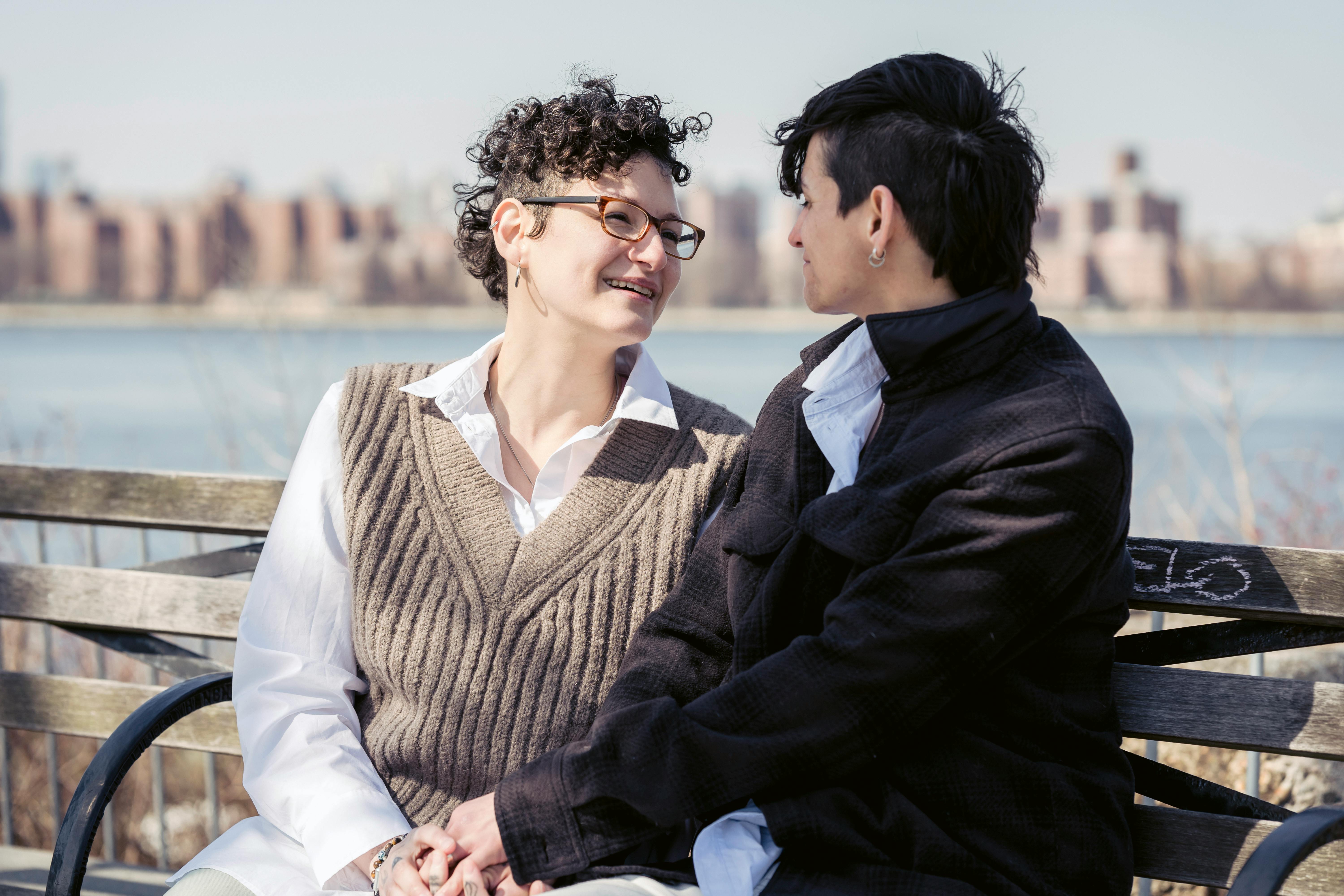 beloved girlfriends holding hands and smiling on river bank in city