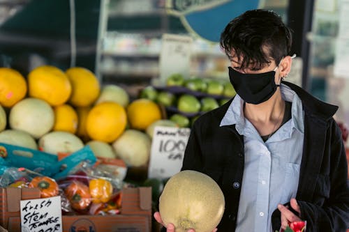 Pensive female in protective mask choosing fruits in market