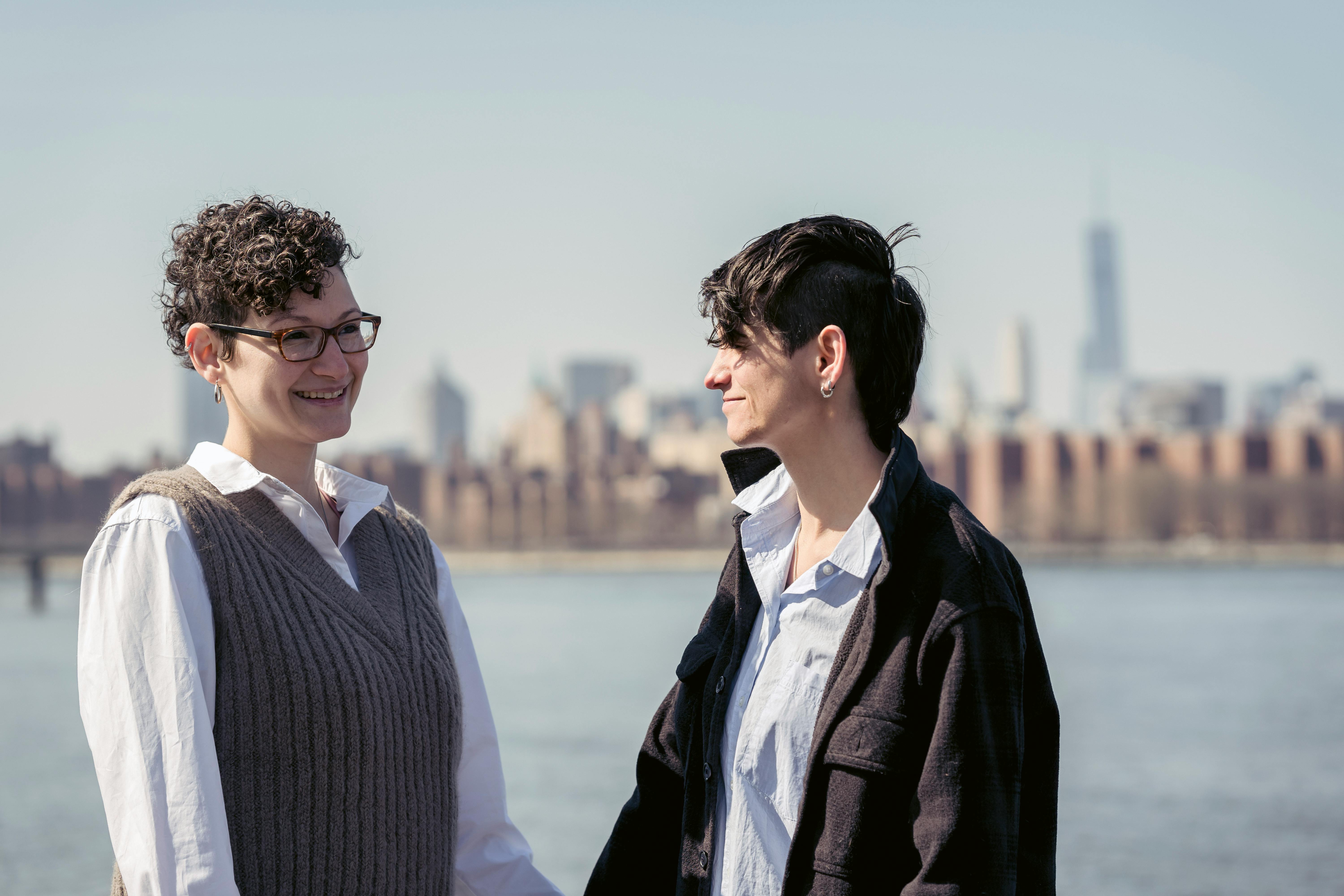 positive lesbian couple holding hands and smiling while chilling at riverside in city