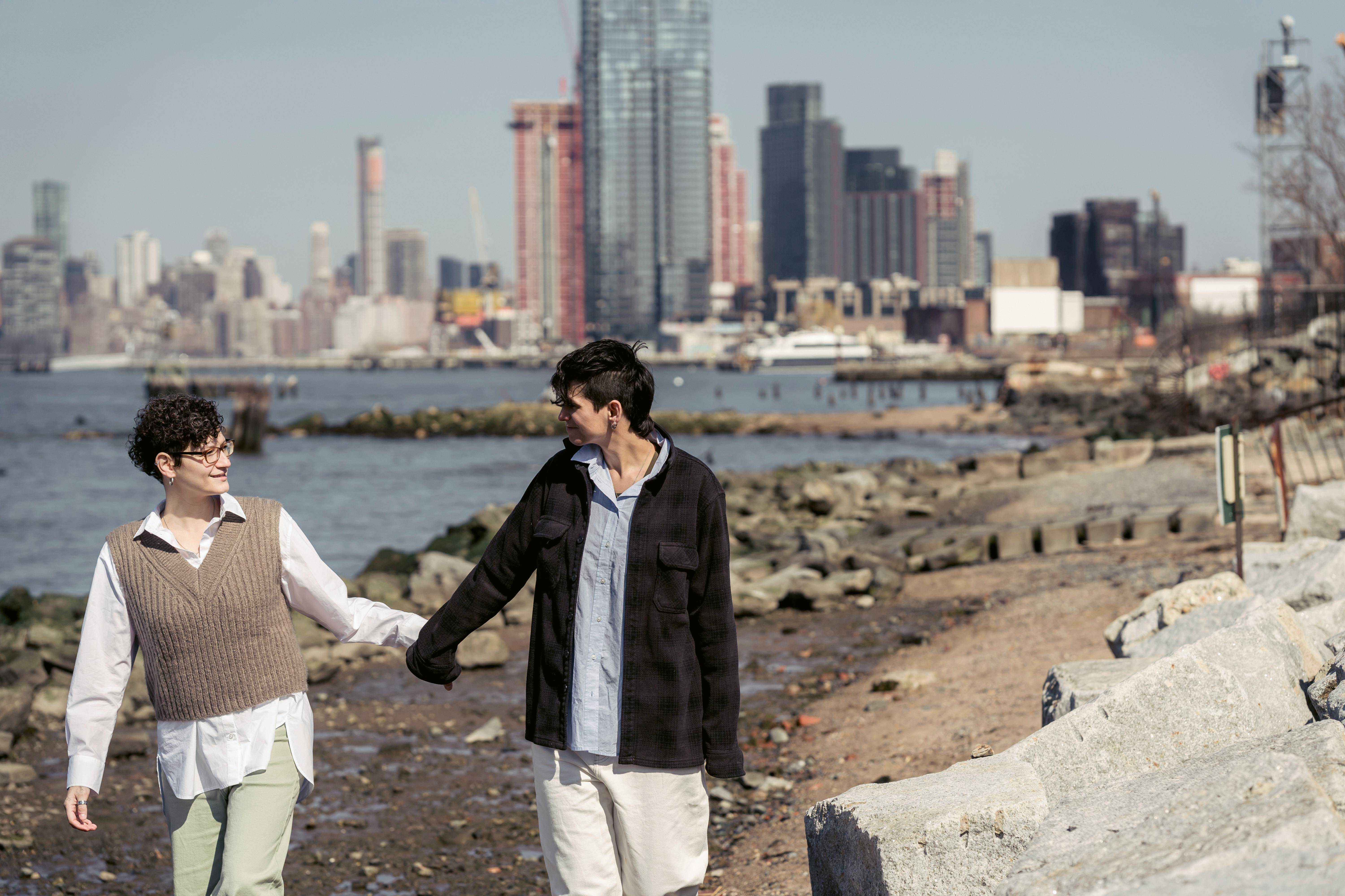 enamored lesbians holding hands while walking on river embankment in city