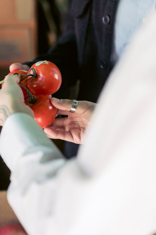 Crop anonymous female customer in casual clothes examining red tomatoes while making purchases in grocery market in daylight