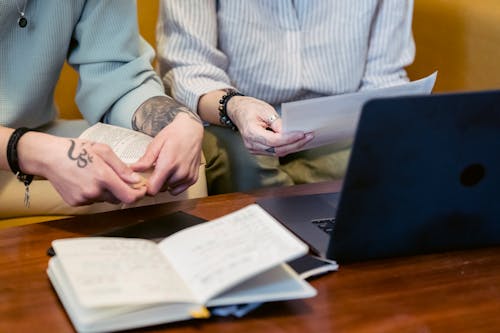 Crop unrecognizable coworkers reading reports at table with netbook