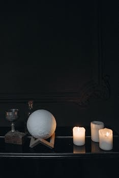 A dark, mystical candlelit arrangement featuring an orb, chalice, and lit candles in an atmospheric setting.
