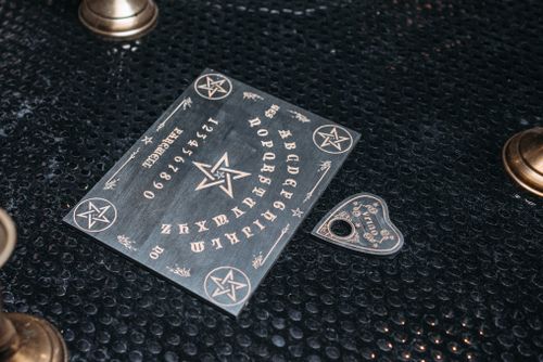 Free A mystical Ouija board setup with candles on a dark textured surface. Stock Photo