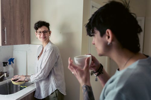 Positive young woman washing fruits and talking with girlfriend drinking coffee