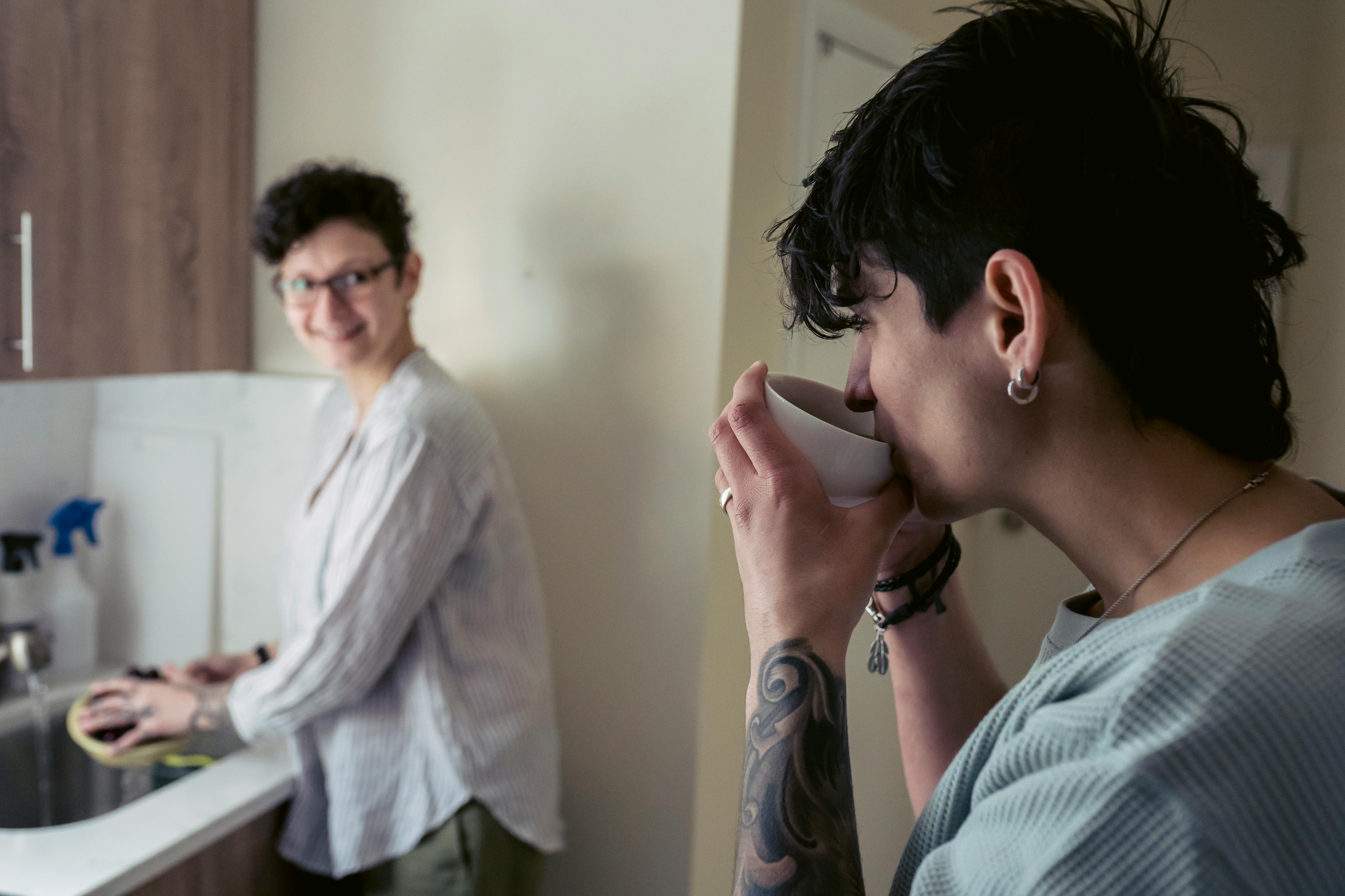 informal woman drinking coffee and chatting with friend in kitchen