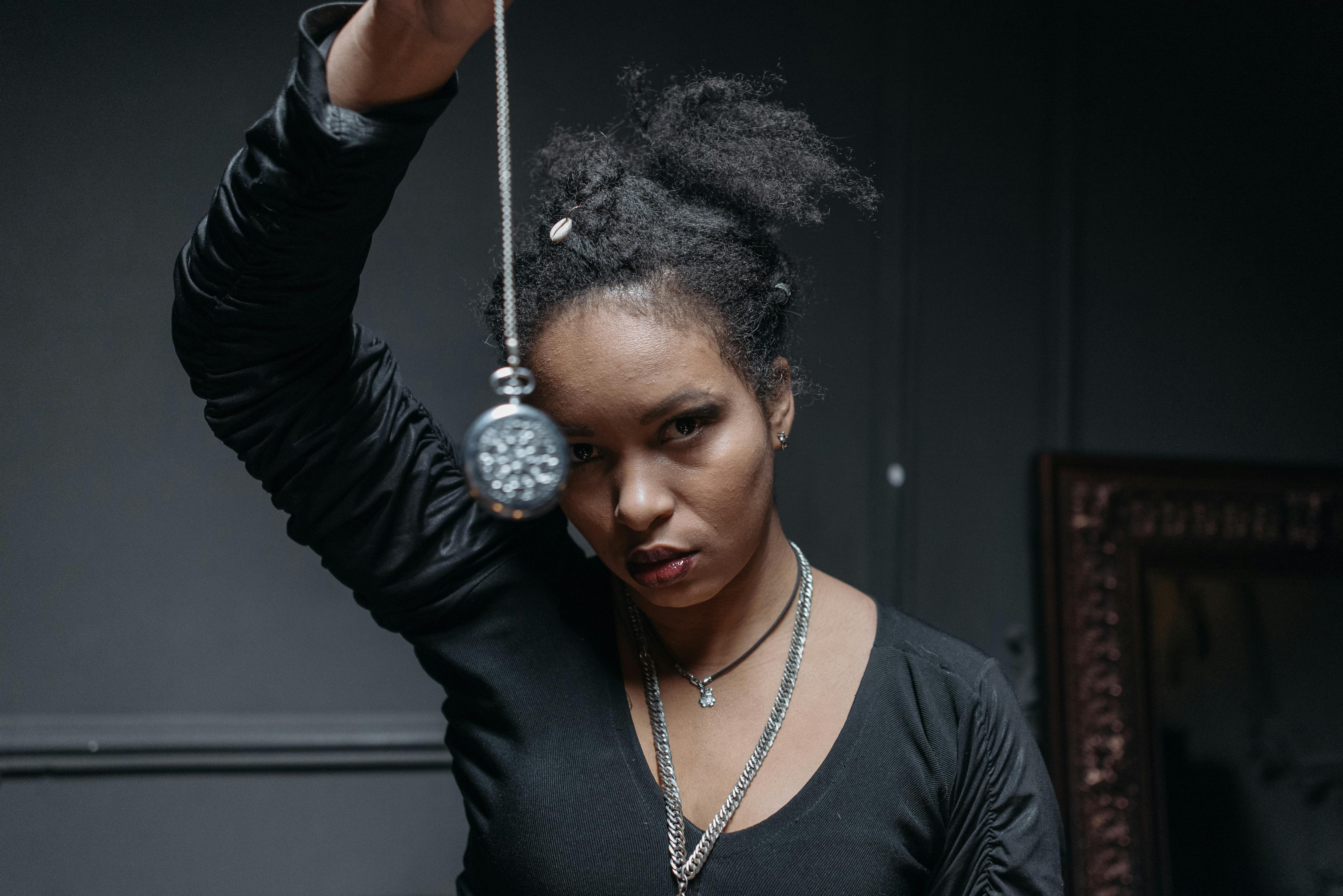 A black woman conducting a spiritual ritual indoors with a pendant, evoking mystical themes.