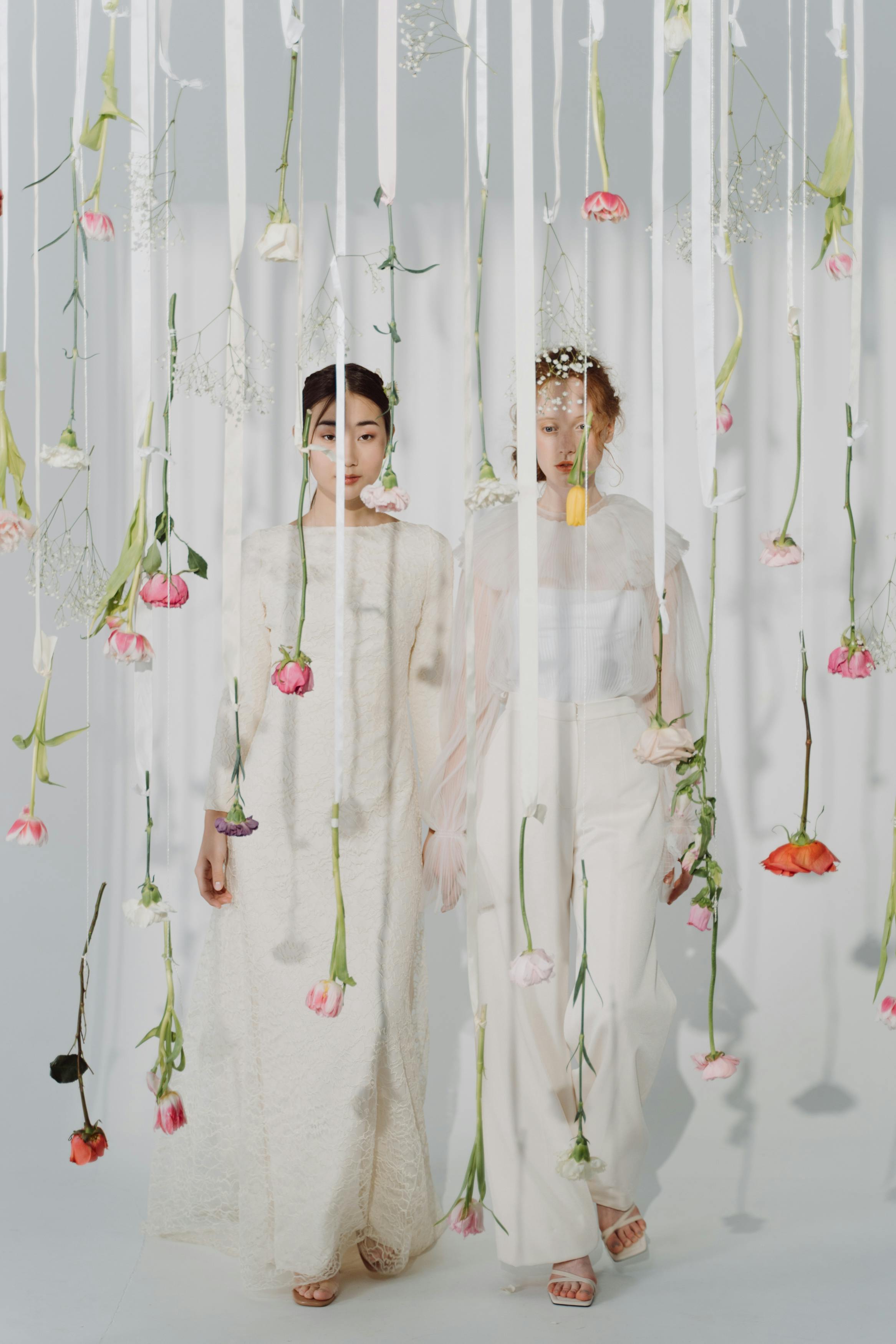 two women in white clothes behind hanging fresh flowers