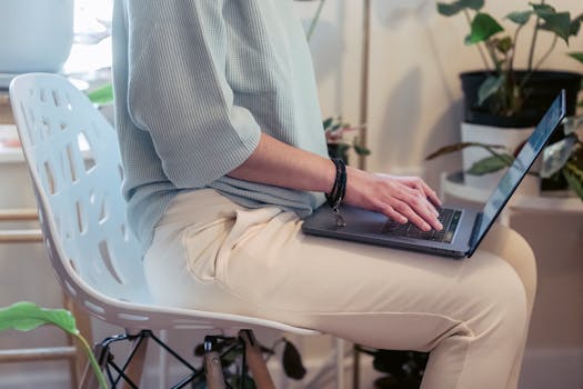 Person working remotely on a laptop at home in a casual setup with potted plants.