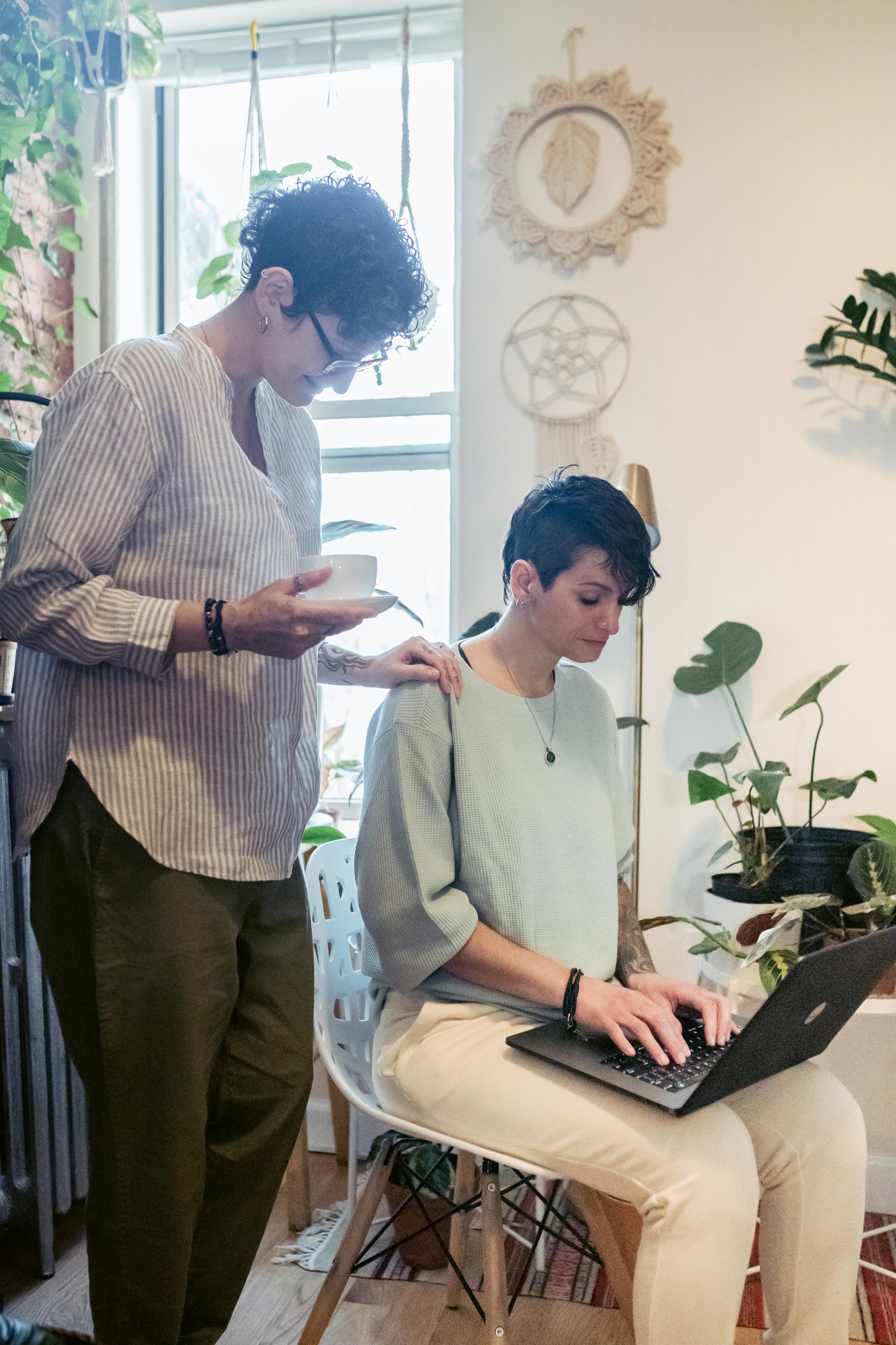 young lesbian woman touching shoulder of girlfriend working remotely on laptop