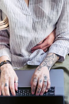 High angle of crop faceless remote worker with tattoos embraced by girlfriend reading book working on netbook
