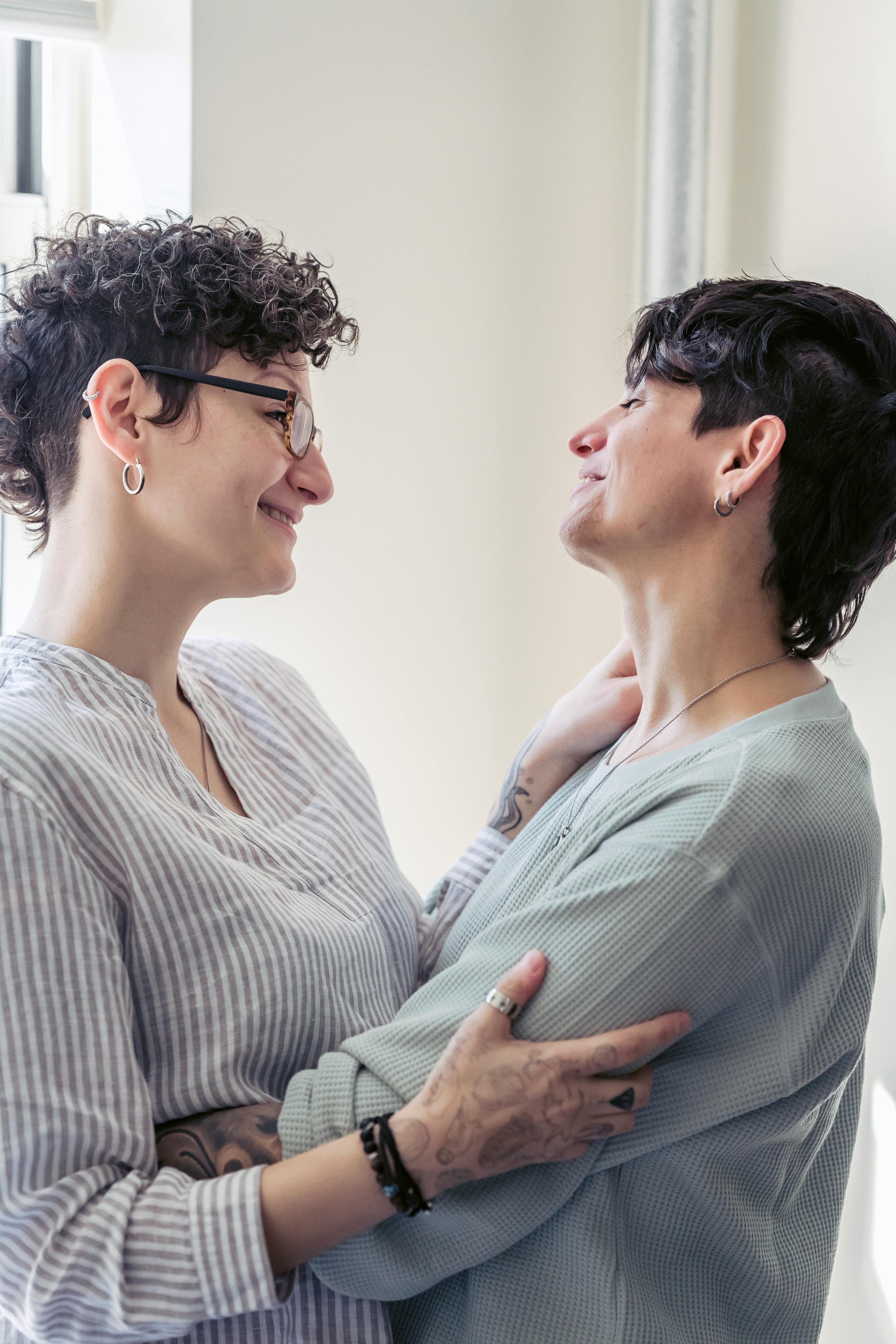 cheerful lesbian women embracing while speaking at home