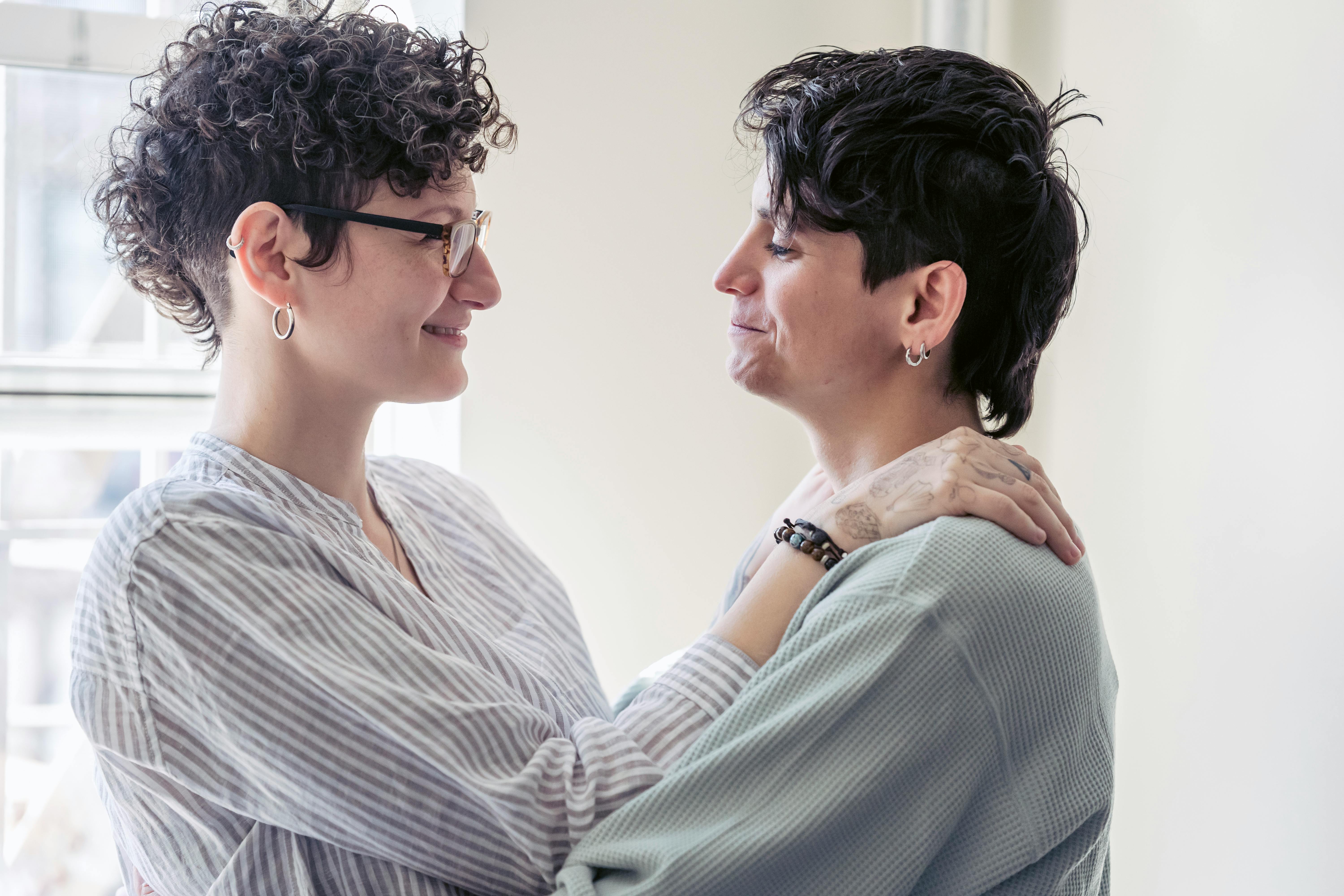 smiling homosexual couple embracing in house room