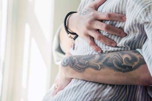 Faceless couple with tattoos embracing at home