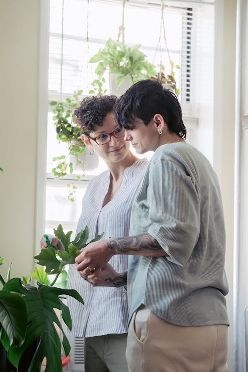 Smiling woman speaking with lesbian partner with tattoo against exotic plants in pots in house room