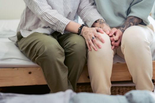 Crop unrecognizable couple in casual wear with tattoos supporting each other while sitting on bed at home